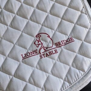 Saddle pad with a red lions bridge logo in the corner.